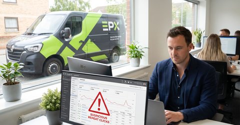 Marketing analyst reviewing a Google Ads dashboard on a laptop flagging a fraud alert on suspicious repeat clicks, with a branded epoxy flooring service van visible outside the office window.