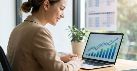 Small business owner smiling while reviewing an upward-trending marketing performance chart on a laptop in a bright office, illustrating steady growth in Google Ads results over time.