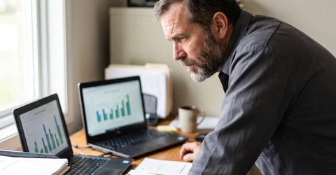 HVAC business owner comparing two laptop screens showing marketing performance charts at his office desk.